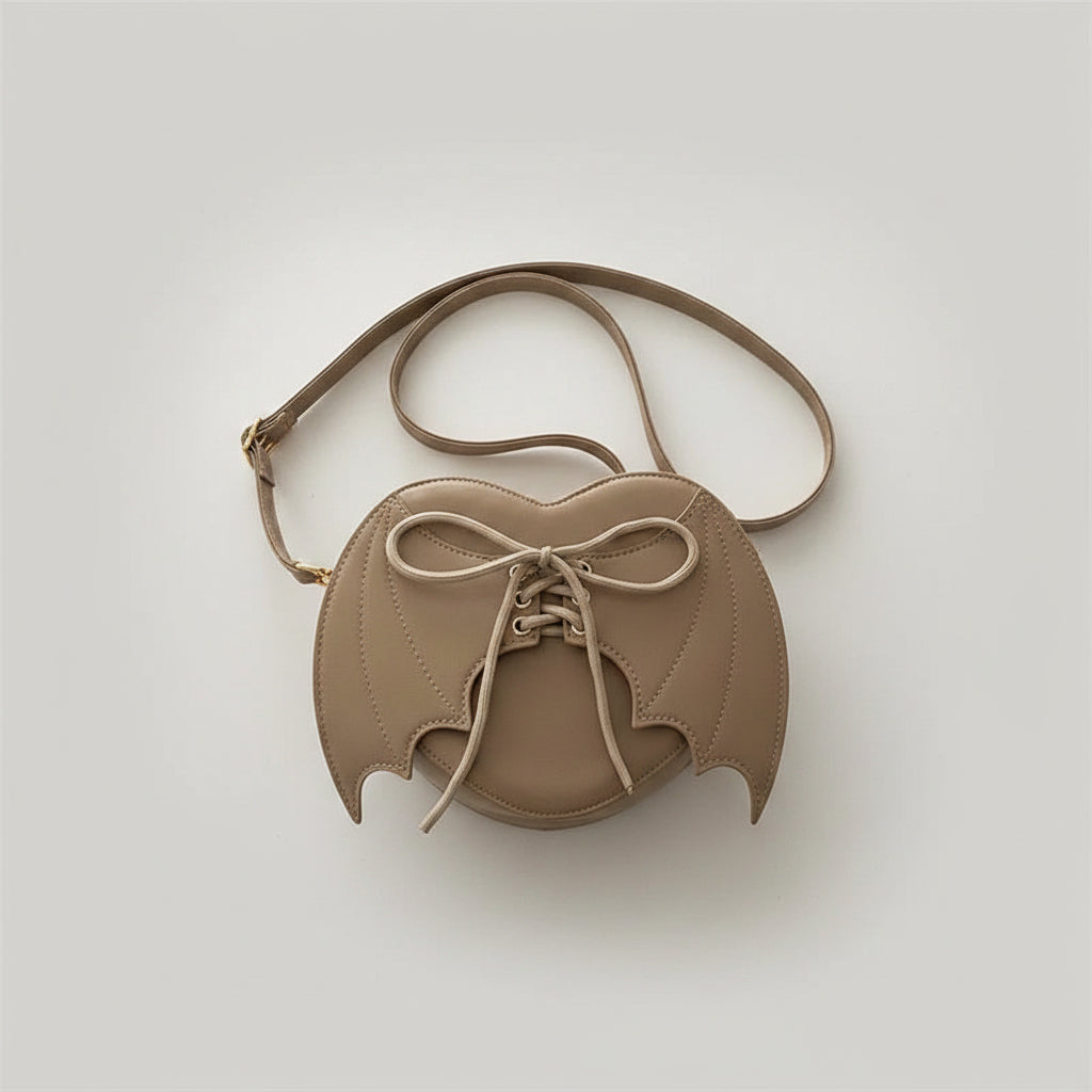 Beige bat-wing shaped crossbody bag with lace-up detail, on denim jacket background