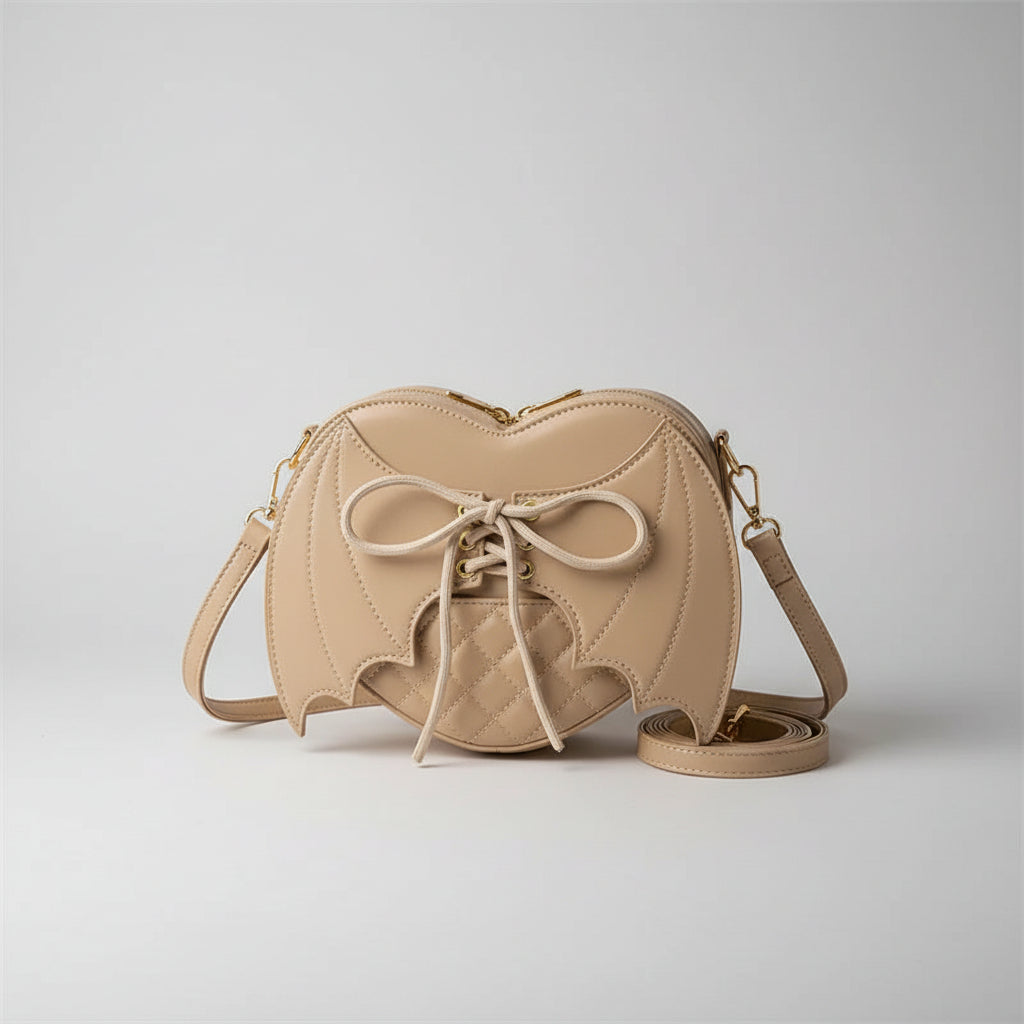 Beige heart-shaped crossbody bag with bat wing design and lace-up front, displayed indoors