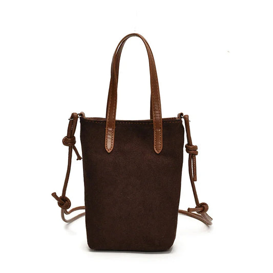 Small brown suede handbag with double handles and adjustable shoulder strap on white background