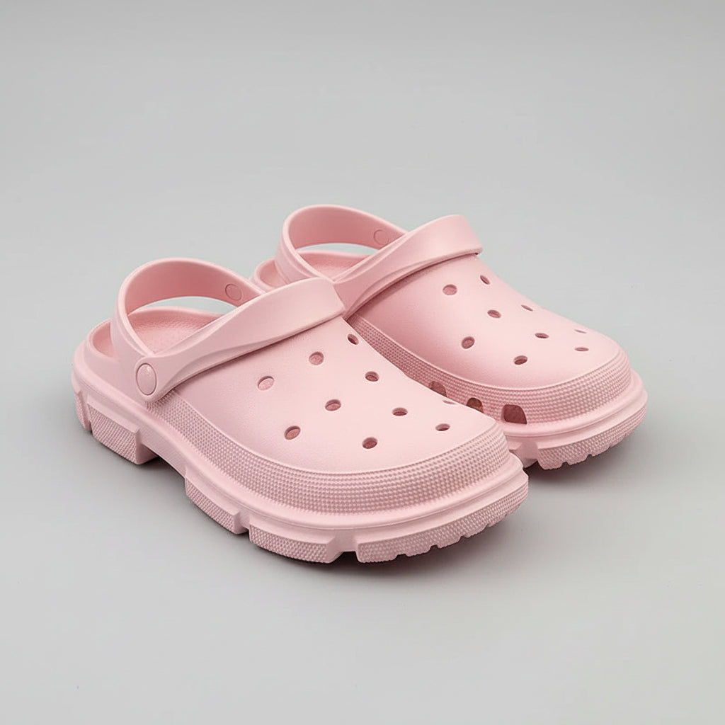 Light pink slip-on foam clogs with ventilation holes, displayed on a wooden surface